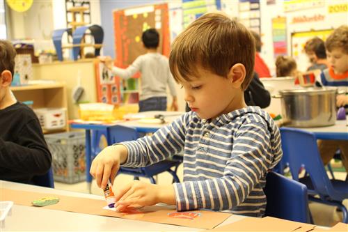 Preschool student putting glue on paper 